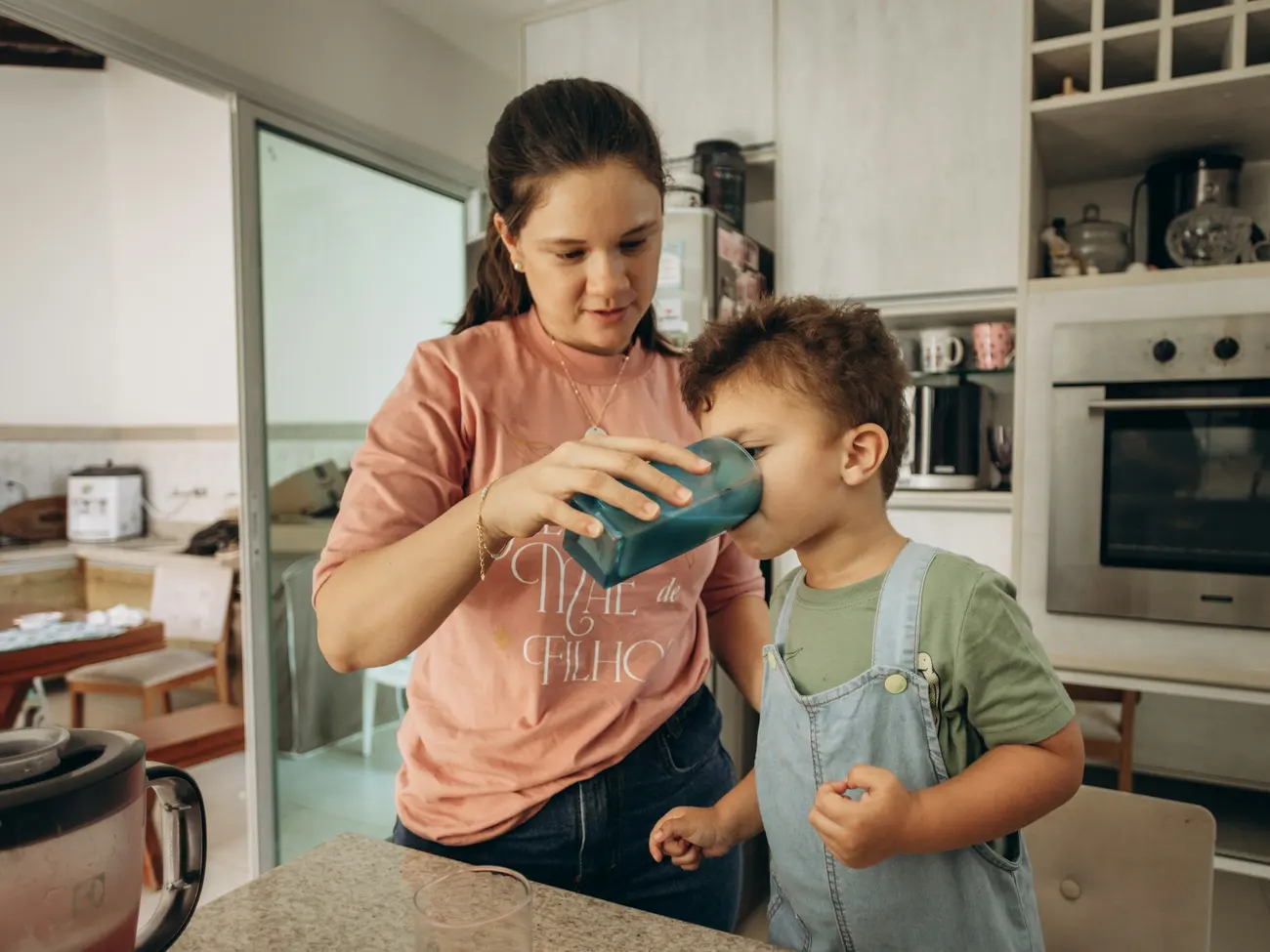 Mãe dando um copo de água para o filho na cozinha de casa